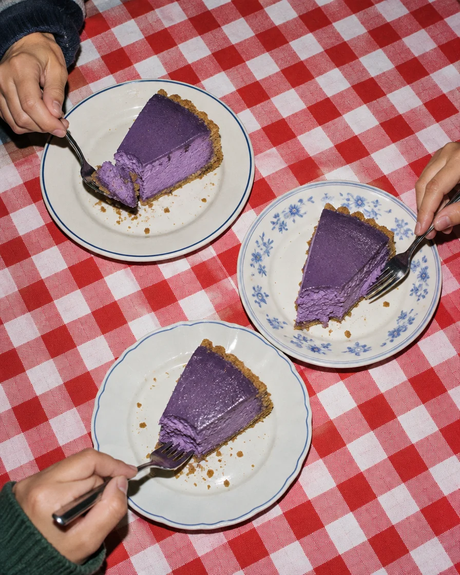Three plates with slices of ube cheesecake on a checked tablecloth