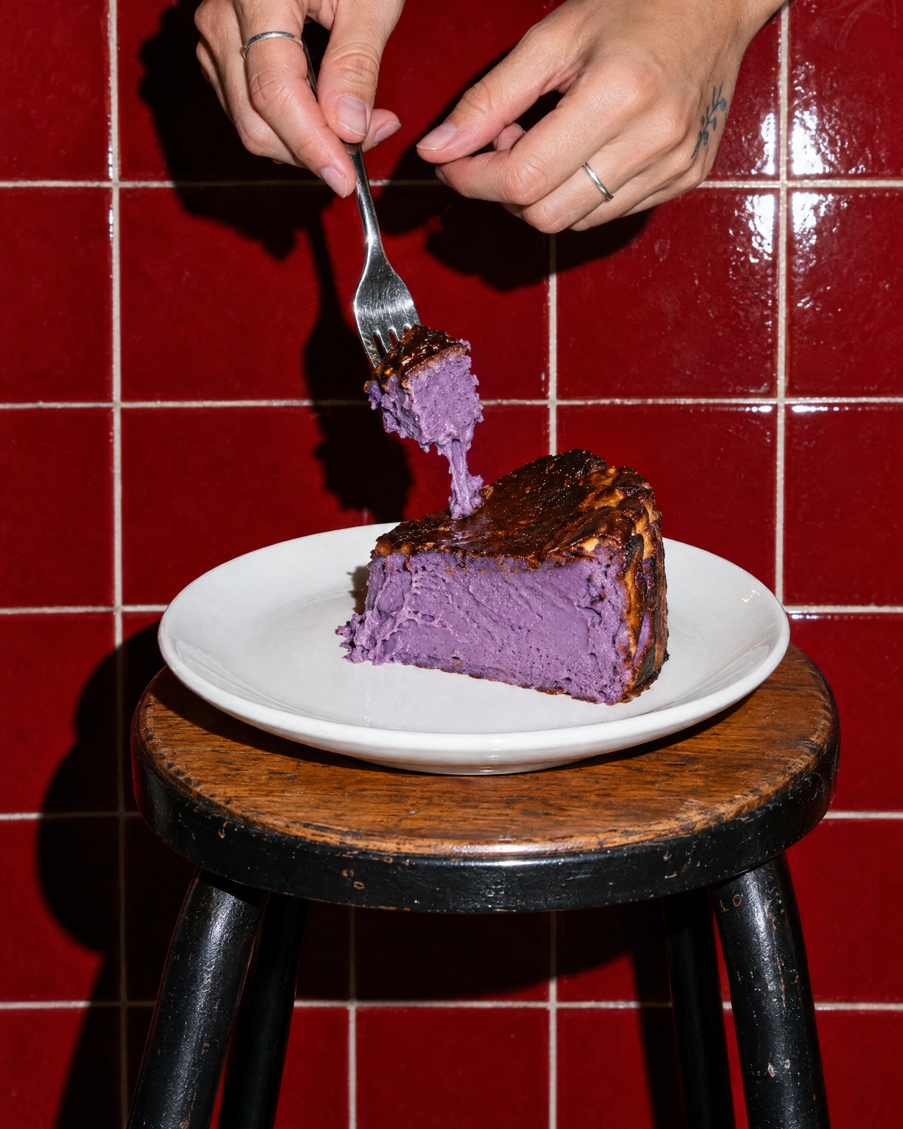 A fork lifting a bite from a slice of ube cheesecake on a white plate
