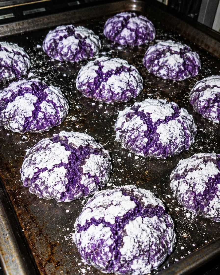 A tray of freshly baked ube crinkle cookies with cracked icing sugar tops