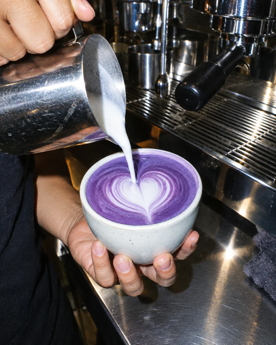 Barista gießt Milchschaum in eine Tasse Ube Latte