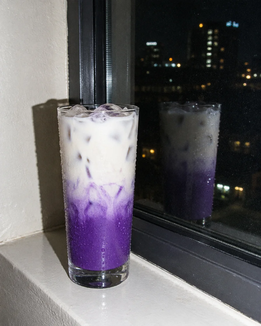 Hohes Glas Iced Ube Latte auf einer Fensterbank am Abend